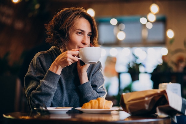 Giovane donna che mangia i croissant ad un caffè