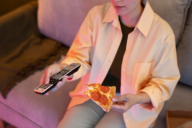 Giovane donna che mangia pizza e che guarda la tv