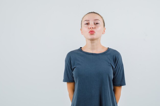 Giovane donna che mantiene le labbra piegate in maglietta grigia e sembra adorabile