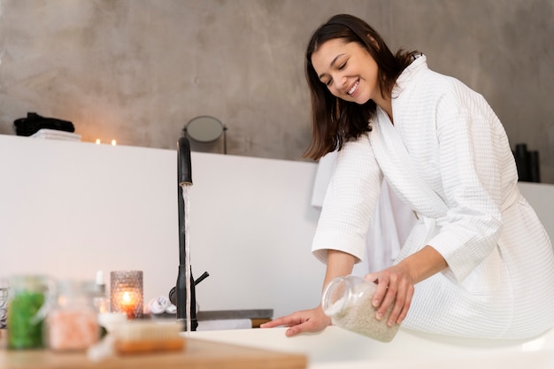 Giovane donna che mette il sale da bagno nell'acqua prima di fare il bagno