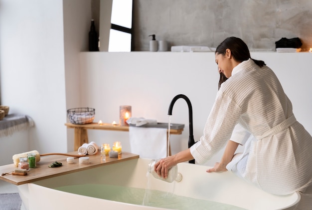 Giovane donna che mette il sale da bagno nell'acqua prima di fare il bagno