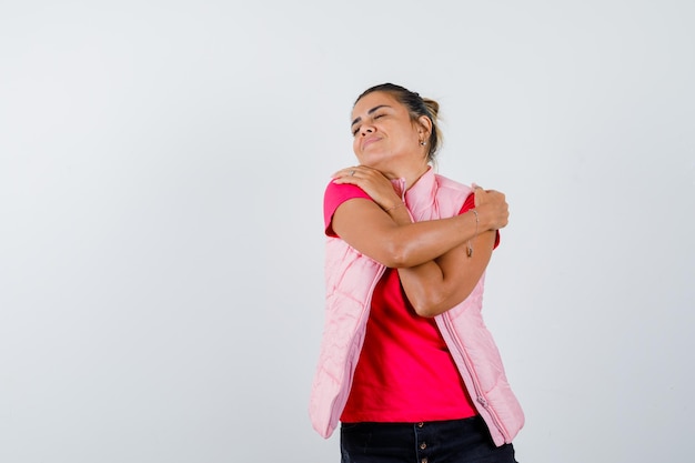 Giovane donna che mette le mani sulle spalle in maglietta e giacca rosa e sembra calma