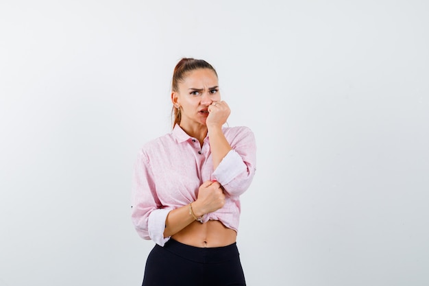 Giovane donna che morde il pugno emotivamente in camicia e sembra spaventata. vista frontale.