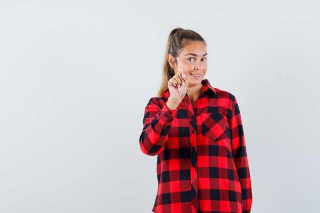 Giovane donna che mostra attesa su un gesto minuto con il dito in alto in camicia casual e guardando fiducioso, vista frontale.