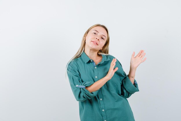 Giovane donna che mostra gesto di benvenuto in camicia verde e sembra sicura