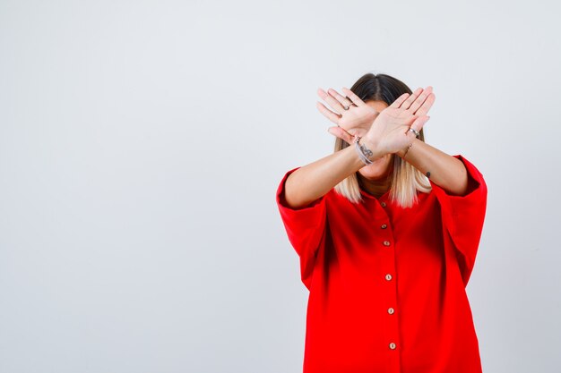 Giovane donna che mostra gesto di rifiuto in camicia rossa oversize e sembra sicura, vista frontale.