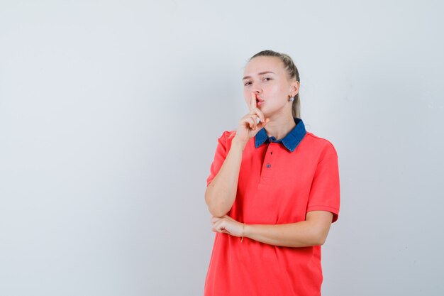 Giovane donna che mostra gesto di silenzio in maglietta e guardando attento