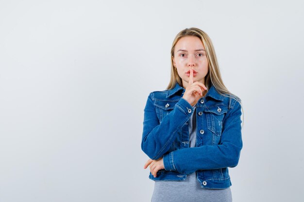 Giovane donna che mostra gesto di silenzio in maglietta, giacca di jeans, gonna e sembra sicura and