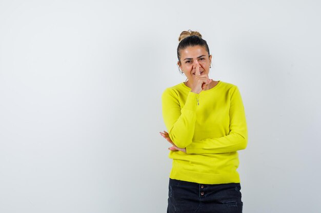 Giovane donna che mostra gesto di silenzio in maglione, gonna di jeans e sembra felice