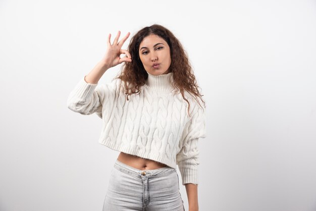 Giovane donna che mostra gesto giusto in maglione bianco con capelli ricci. Foto di alta qualità