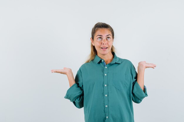 Giovane donna che mostra gesto impotente in camicia blu e che sembra confusa