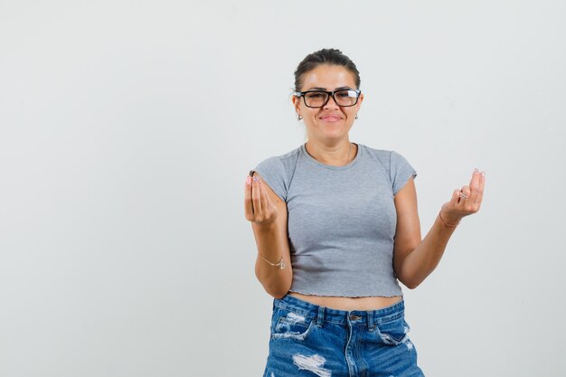 Giovane donna che mostra gesto italiano in t-shirt, pantaloncini e allegro.