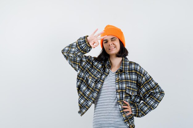 Giovane donna che mostra gesto ok in camicia a scacchi cappello arancione che sembra carina