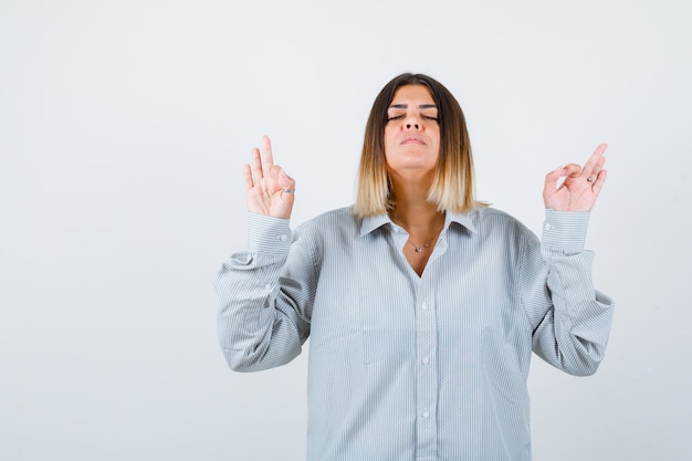 Giovane donna che mostra gesto ok in camicia oversize e sembra pacifica. vista frontale.