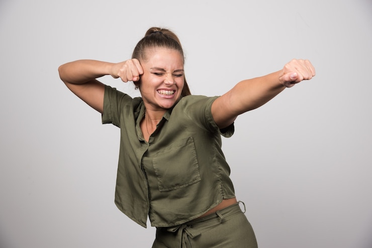 Foto gratuito giovane donna che mostra i suoi pugni sul muro grigio.