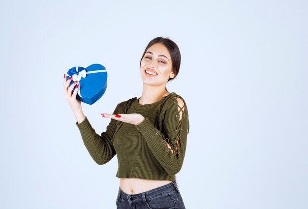 Giovane donna che mostra il contenitore di regalo blu su fondo bianco.