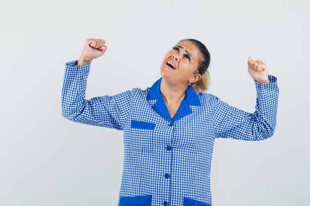 Giovane donna che mostra il gesto del vincitore in camicia del pigiama a quadretti blu e sembra carina. vista frontale.