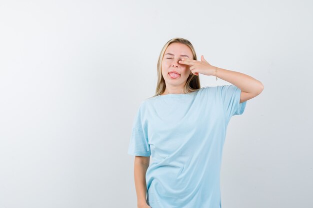 Giovane donna che mostra il gesto della pistola mentre sporge la lingua in t-shirt e sembra carina, vista frontale.