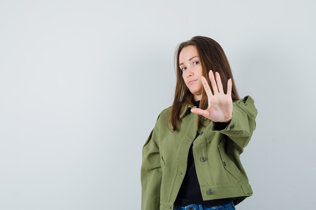 Giovane donna che mostra il gesto di arresto in giacca verde e guardando attento. vista frontale.