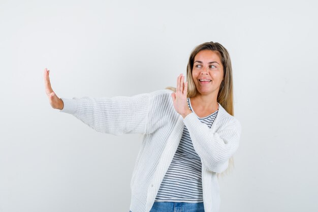 Giovane donna che mostra il gesto di arresto in t-shirt, giacca e sembra felice, vista frontale.