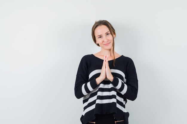 Giovane donna che mostra il gesto di namaste in camicia casual e sembra speranzosa