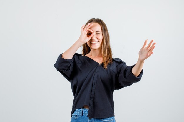 Giovane donna che mostra il gesto giusto sull'occhio in camicia, pantaloncini e sguardo allegro. vista frontale.