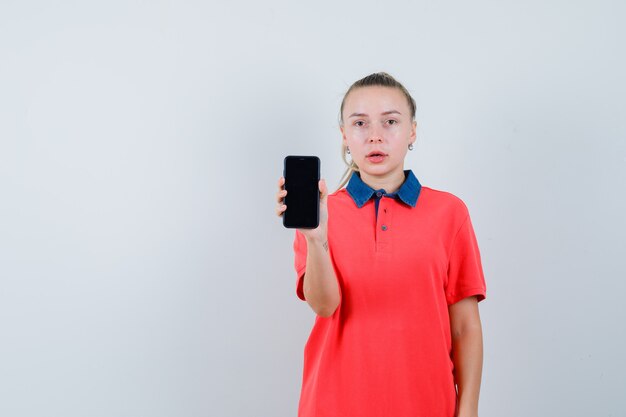 Giovane donna che mostra il telefono cellulare in maglietta e che sembra perplessa