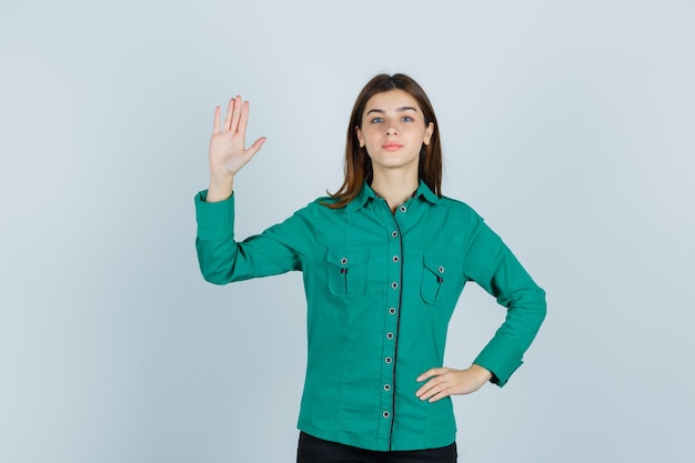 Giovane donna che mostra la palma in camicia verde e guardando fiducioso, vista frontale.
