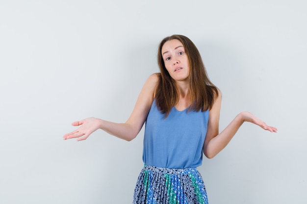 Giovane donna che mostra un gesto impotente alzando le spalle in canottiera, gonna e guardando perplessa