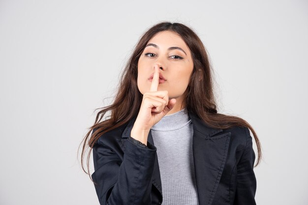 Giovane donna che mostra un segno di gesto di silenzio mettendo il dito in bocca.