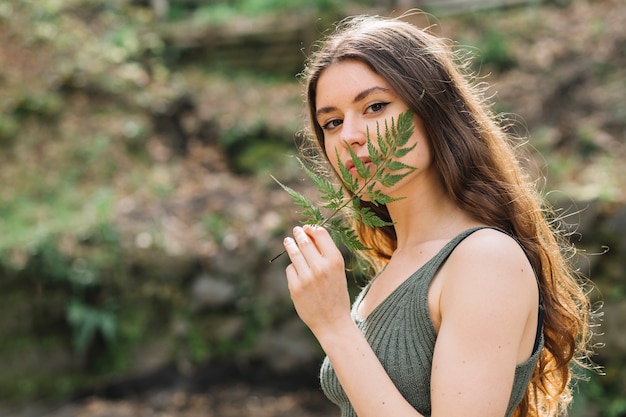 Giovane donna che odora su una foglia nella foresta