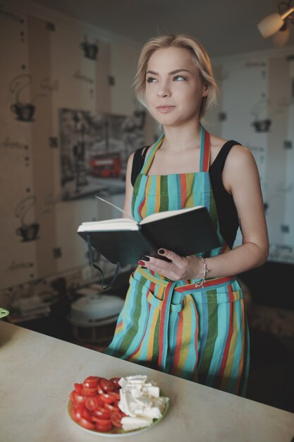 Giovane donna che osserva in su in un libro di ricette