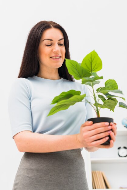 Giovane donna che osserva pianta verde in vaso di fiori