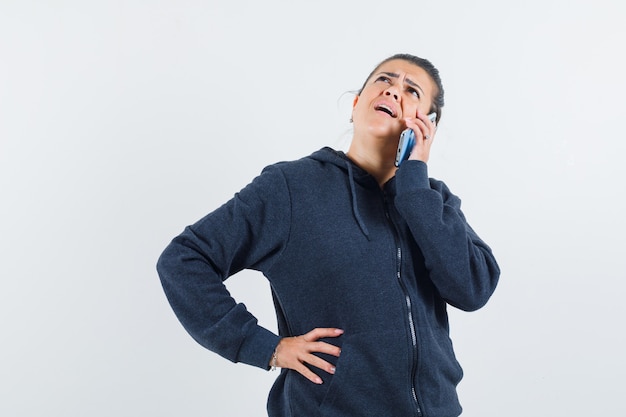 Giovane donna che parla al telefono mentre si tiene la mano sulla vita in giacca e sembra loquace