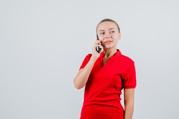 Giovane donna che parla sul telefono cellulare in maglietta rossa e guardando pensieroso