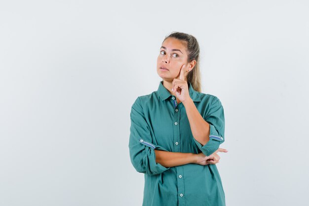 Giovane donna che pensa in camicia blu e che sembra pensieroso