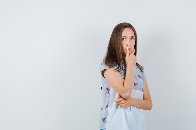 Giovane donna che pensa mentre cerca in t-shirt e sembra esitante. vista frontale.