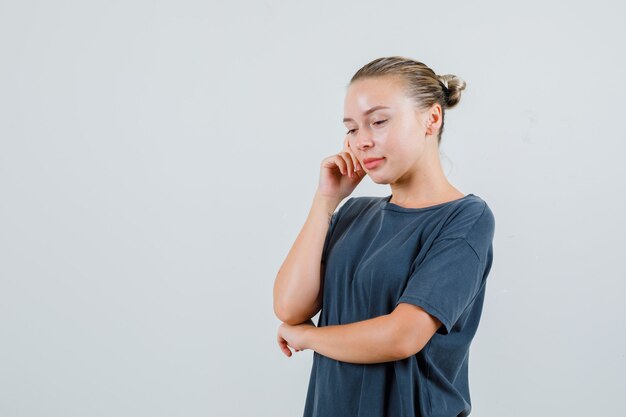 Giovane donna che pensa mentre guarda in t-shirt grigia e sembra speranzosa