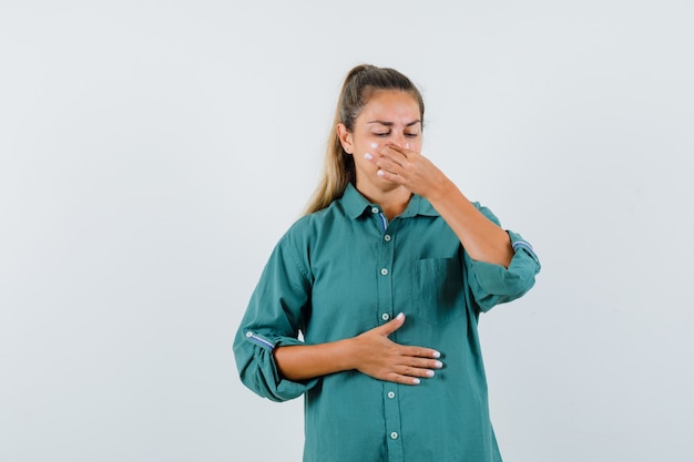 Giovane donna che pizzica il naso a causa del cattivo odore in camicetta verde e sembra esausta