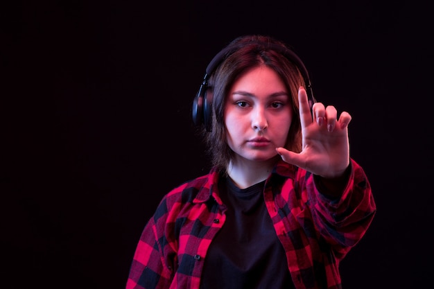 Giovane donna che posa con la camicia rossa e nera a quadretti facendo uso delle cuffie