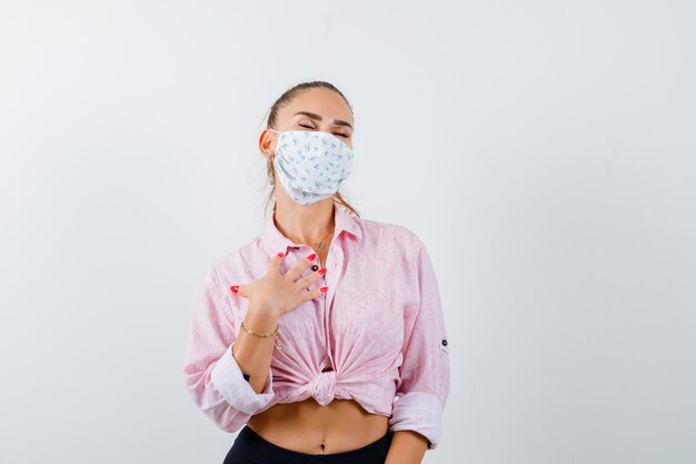 Giovane donna che posa con la mano sul petto in camicia, maschera e sembra rilassata. vista frontale.