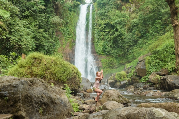 Giovane donna che pratica lo yoga dalla cascata