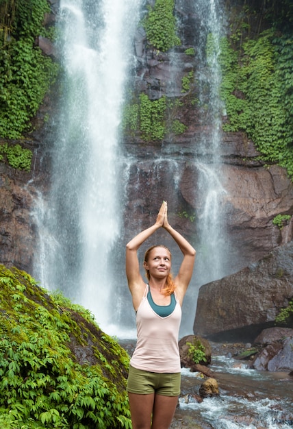 Giovane donna che pratica lo yoga dalla cascata