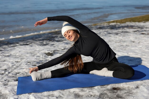 Giovane donna che pratica yoga all'aperto durante l'inverno sulla spiaggia