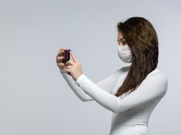 Giovane donna che prende foto se stessa nella maschera medica sterile bianca