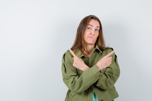 Giovane donna che punta a destra e a sinistra in giacca verde e sembra indecisa, vista frontale.