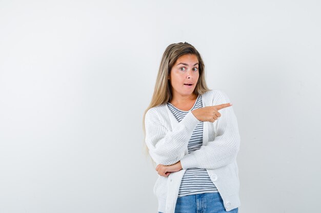 Giovane donna che punta a destra in t-shirt, giacca e sembra curiosa, vista frontale.