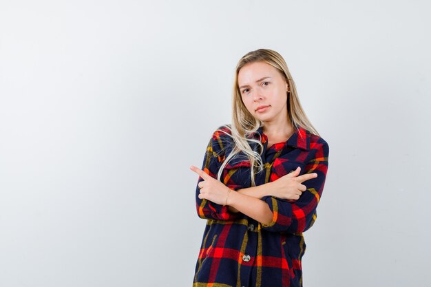 Giovane donna che punta a entrambi i lati in camicia a quadri e sembra esitante. vista frontale.