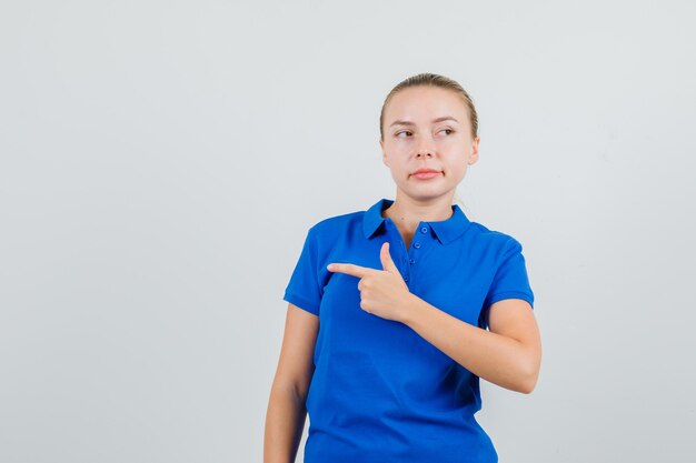 Giovane donna che punta a lato in maglietta blu e che sembra scontenta