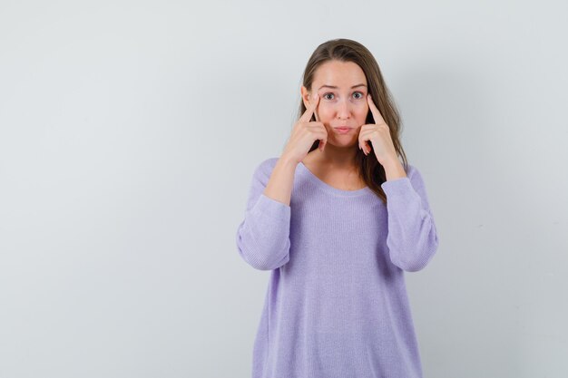 Giovane donna che punta agli occhi in camicetta lilla e che sembra concentrata. vista frontale. spazio per il testo